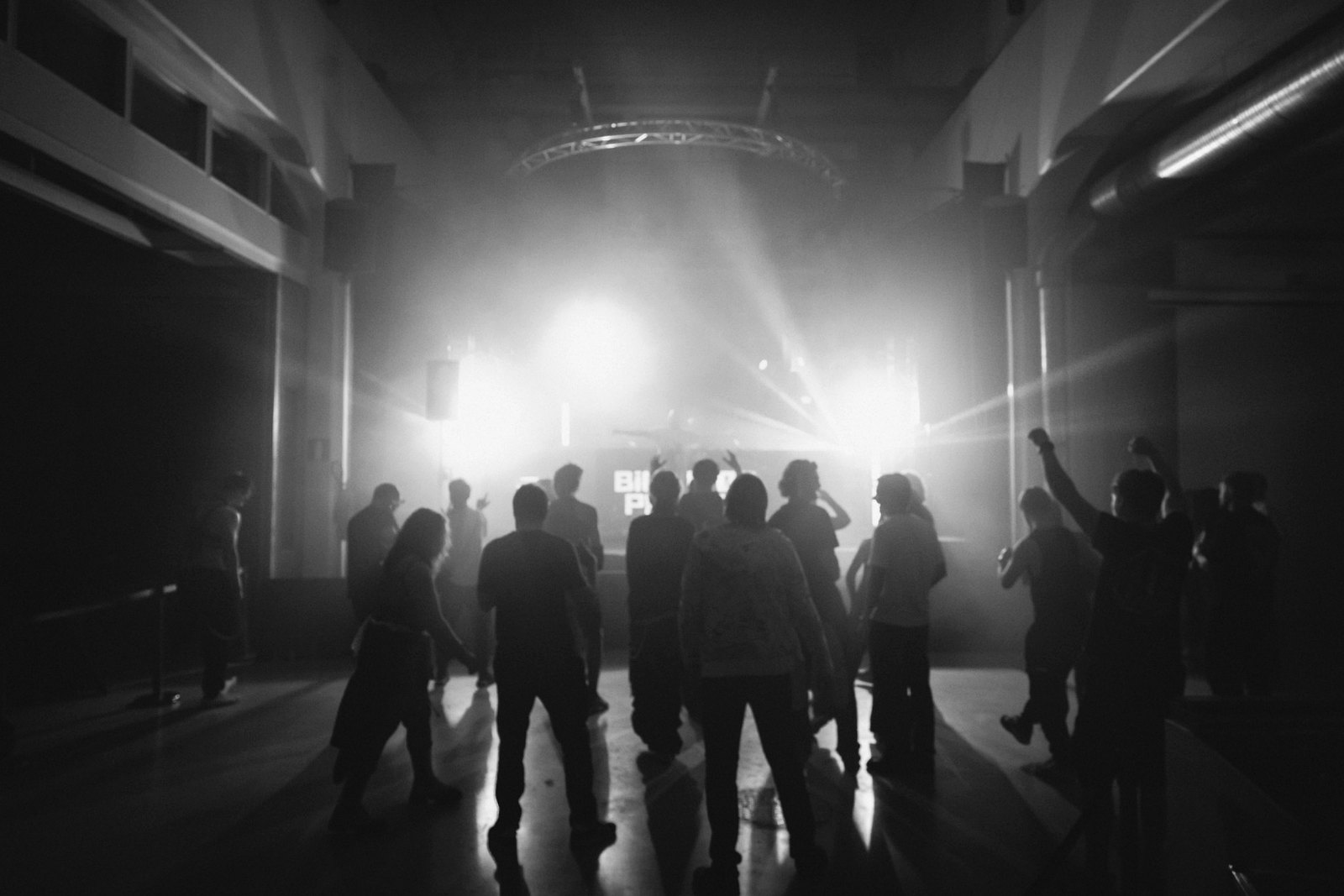 Black and white photograph of a crowd standing in strong stage light.