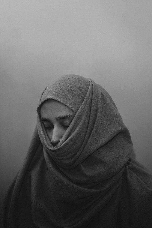 A softly lit monochrome portrait of a person wearing a head covering.