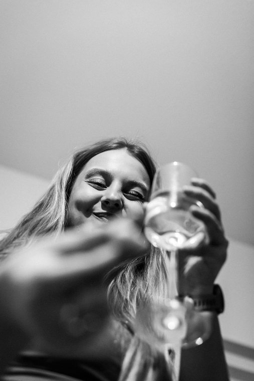 A smiling person pours a drink toward the camera in monochrome.