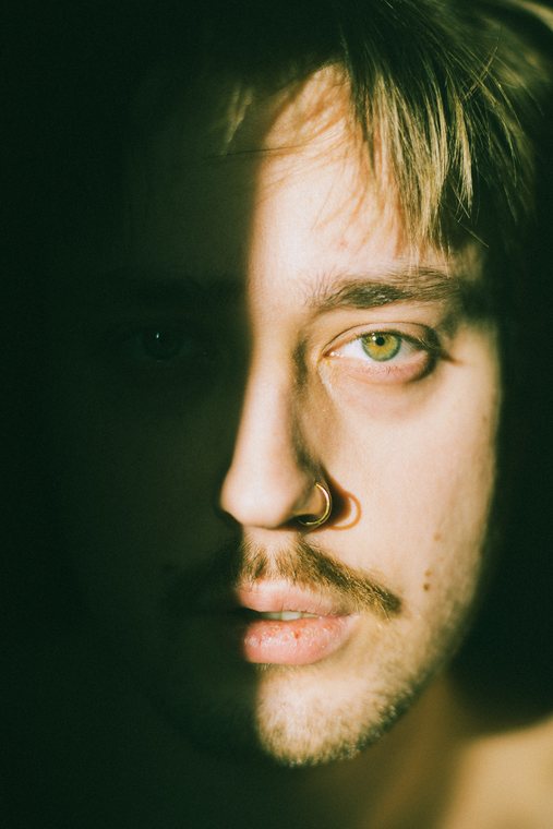 A close portrait emerges from deep green shadow and warm light.