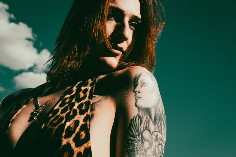 A close portrait places a tattooed shoulder against a saturated blue sky.