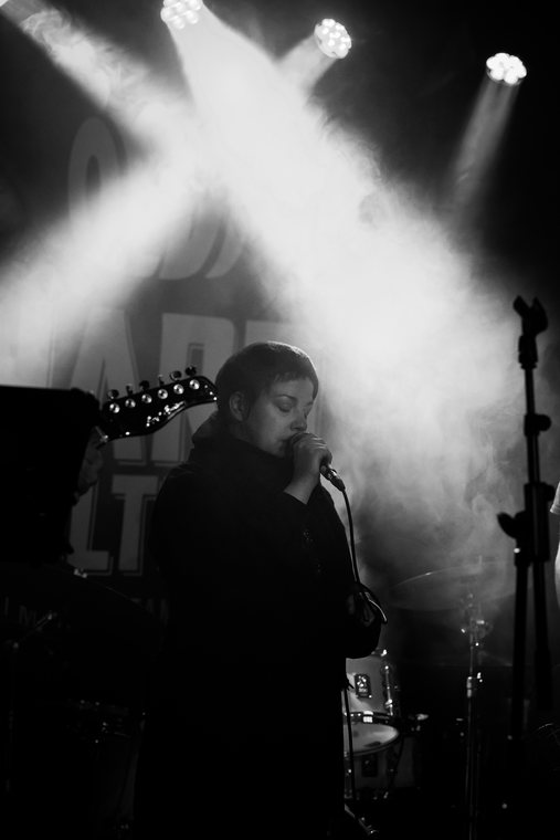 A monochrome musician performing beneath crossing beams of white stage light.